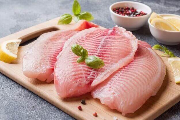 raw fatty fish fillet tilapia cutting board with lemon spices dark table